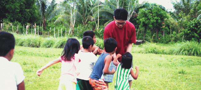 フィリピンの子どもたちに囲まれて遊ぶ、大学生。